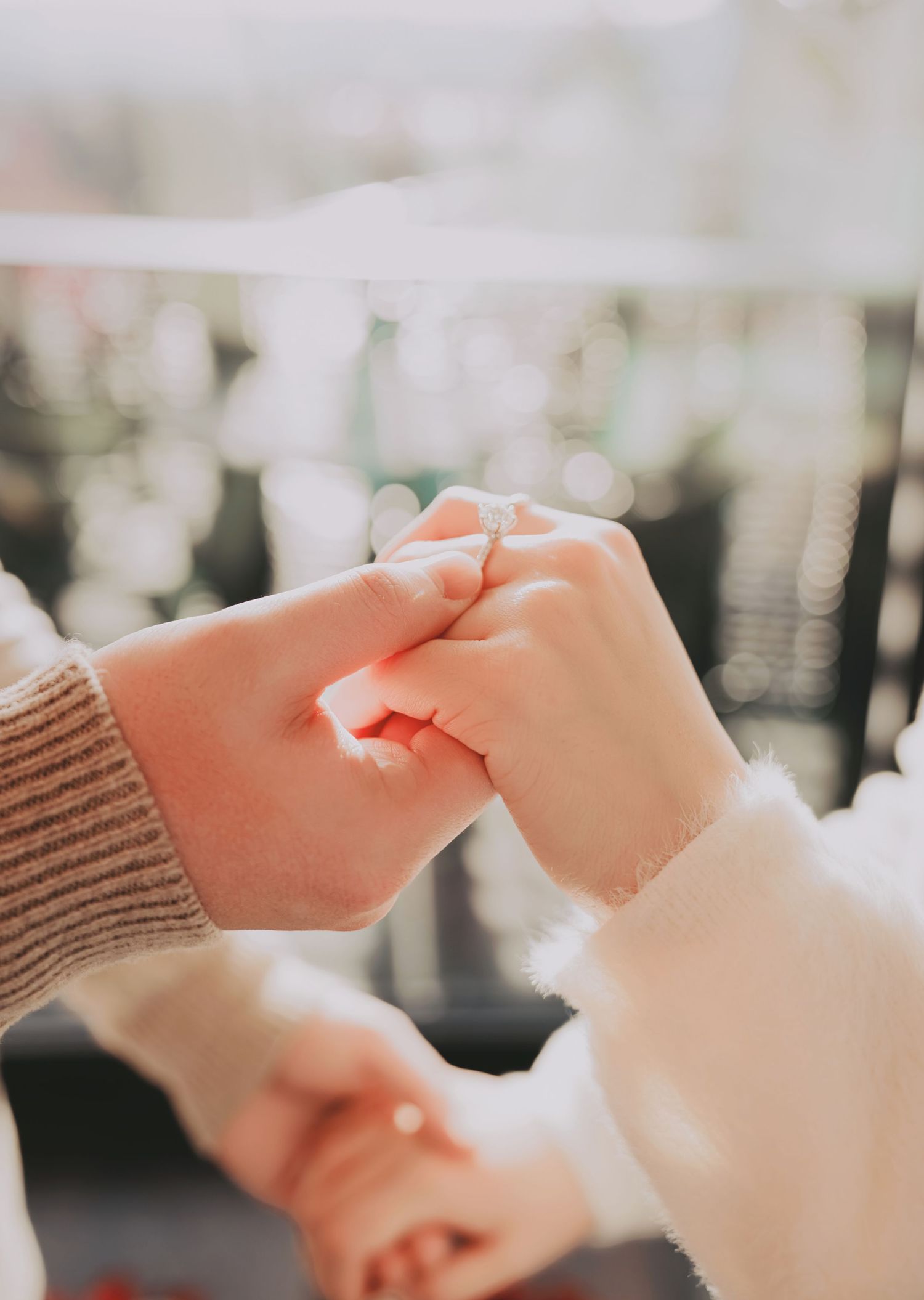 Close-up of a couple holding hands with an engagement ring visible in soft natural light.