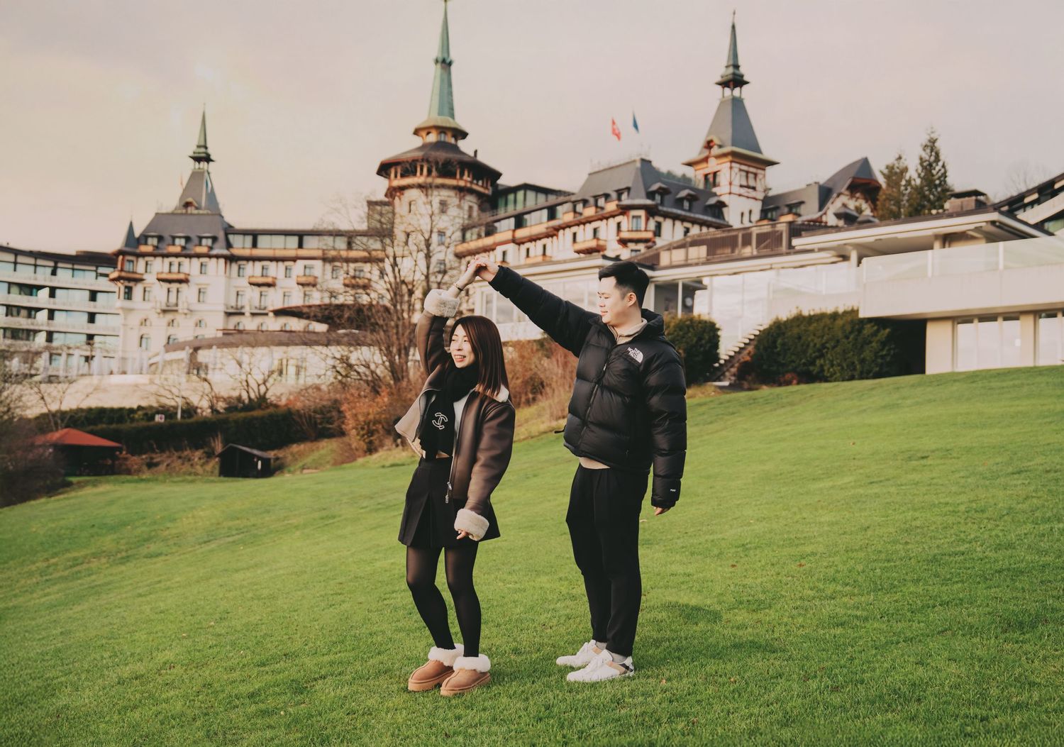 Couple walking on green lawn with stunning European castle hotel backdrop.