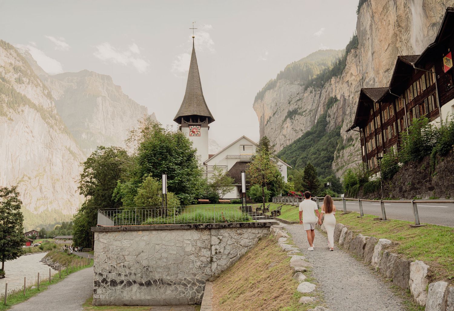 Couple walking toward a historic church with a pointed steeple in a picturesque Swiss mountain town.