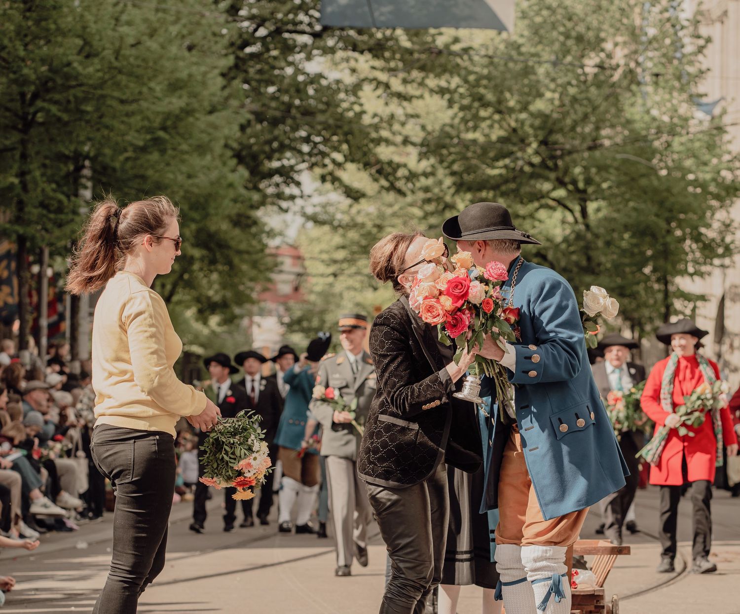 A man in traditional blue Bavarian attire presents pink roses to a woman during an outdoor festival.