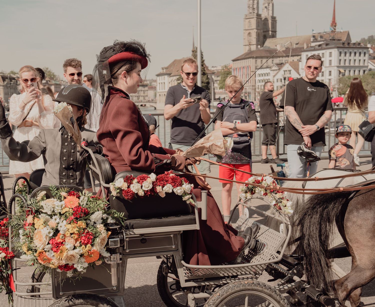 Woman in Victorian costume riding a flower-adorned carriage at a Swiss street festival.