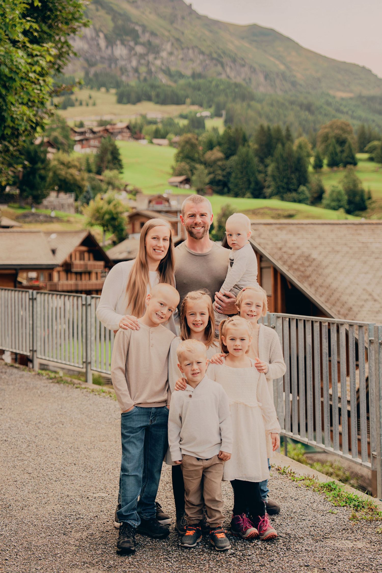 Happy family with parents and six children posing together on a gravel path with Swiss Alps backdrop.