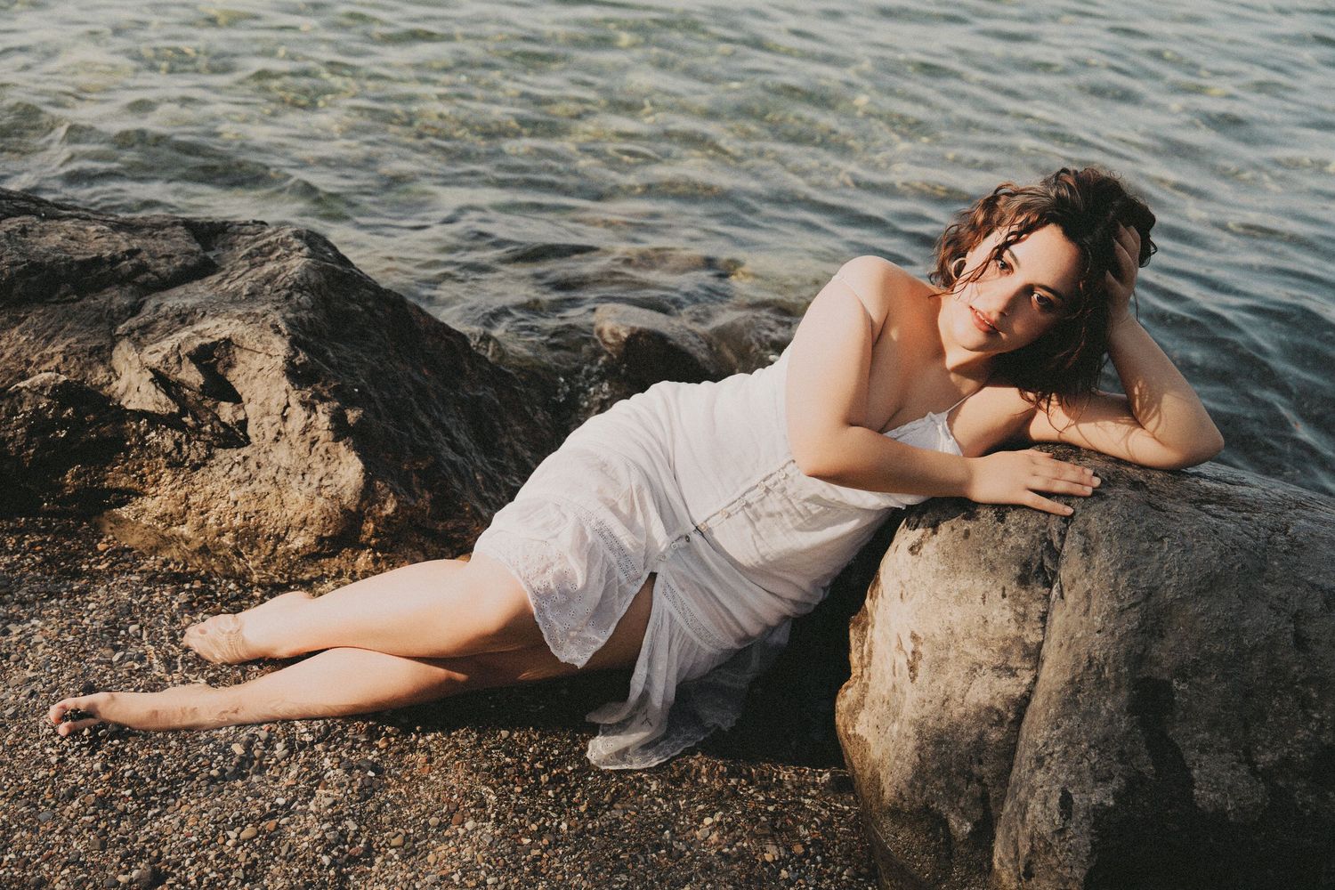 Woman in white dress lying on rocks by the sea.