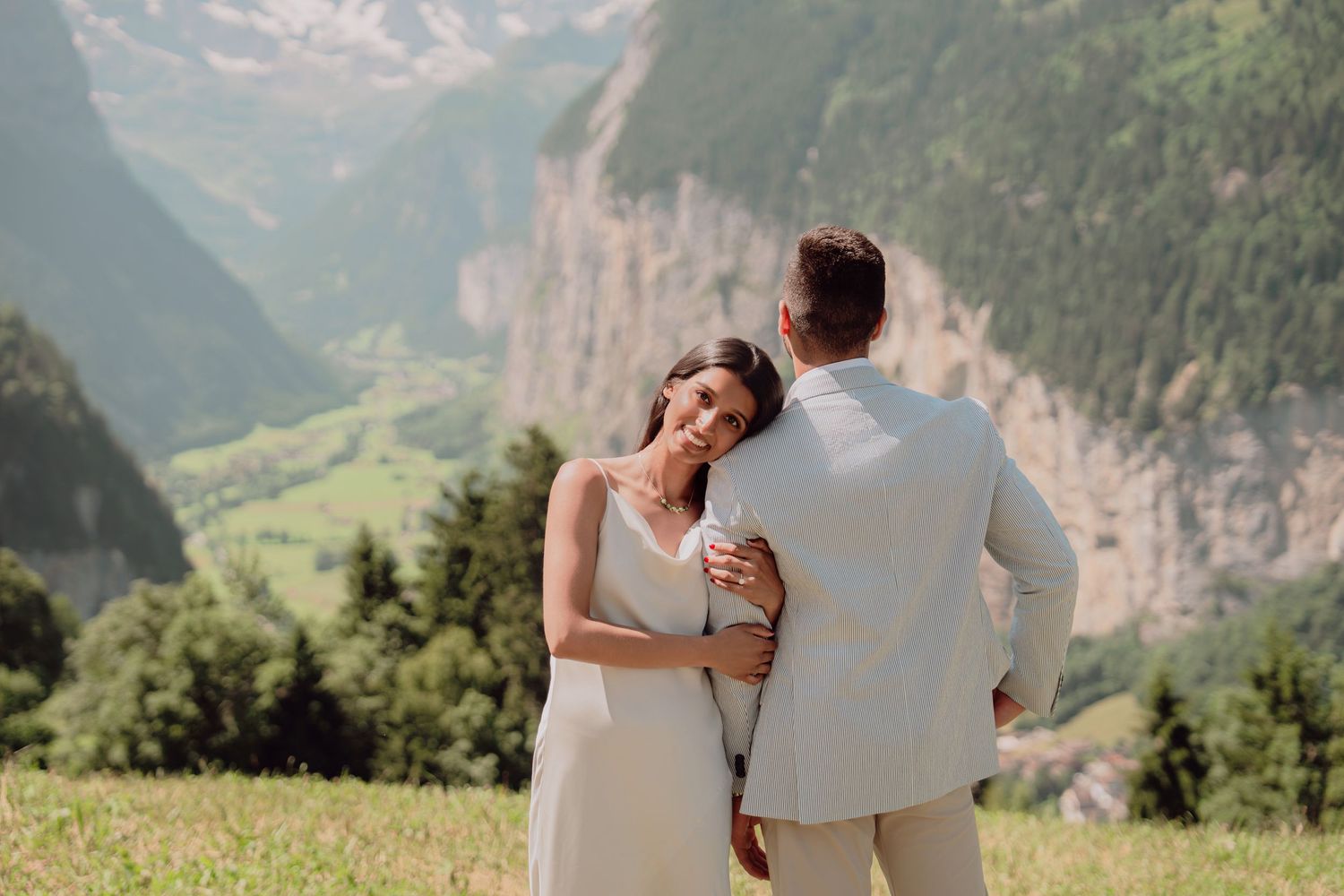Woman smiling while embracing her partner on a scenic alpine meadow with lush Swiss valley views.