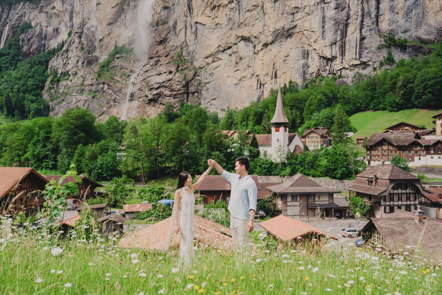 Couple holding hands in a meadow overlooking the stunning Lauterbrunnen village and waterfall in Switzerland.