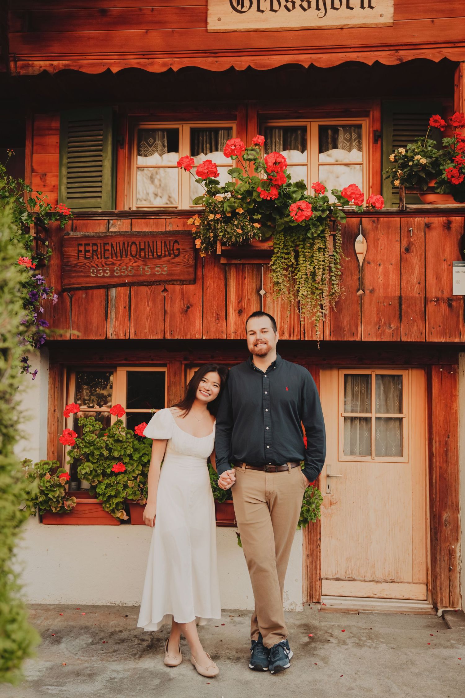 Couple standing hand in hand before the rustic Grosshorn Ferienwohnung chalet in Switzerland.