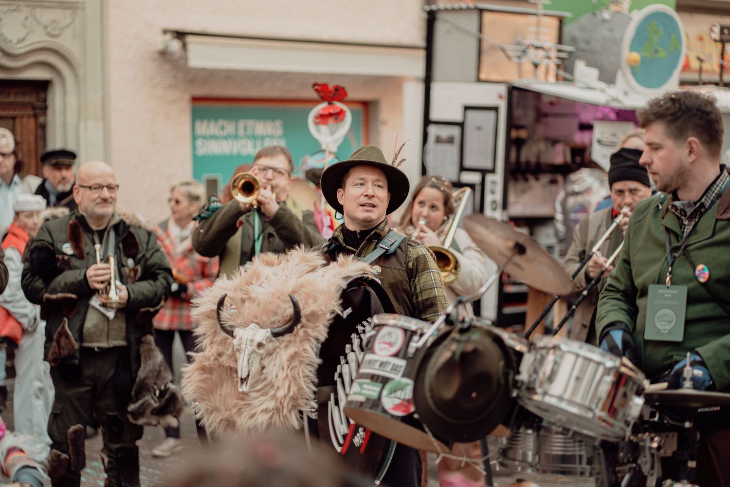 Street performers in traditional costumes playing brass instruments during a lively outdoor festival parade.
