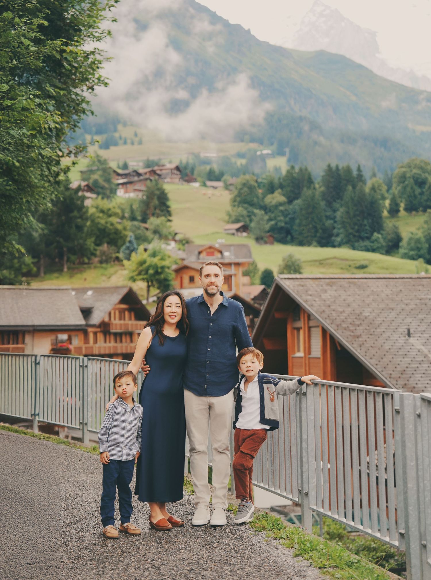 Couple with two young sons posing together on a path with green Swiss Alpine hillside backdrop.