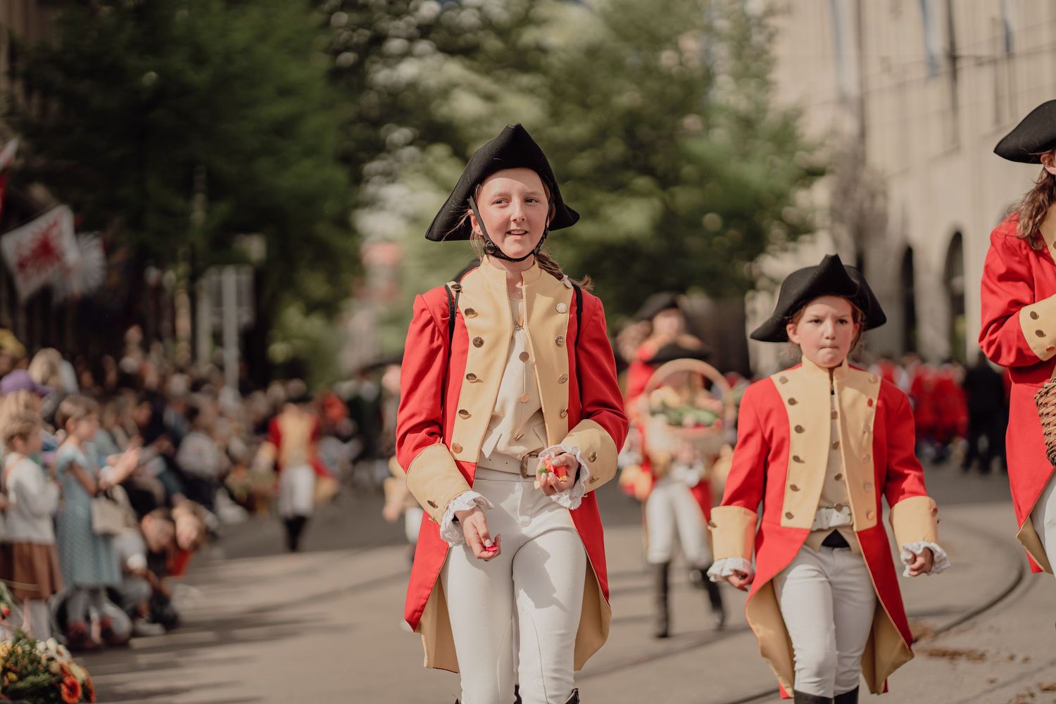 Children and youth in red colonial uniforms march during a festive street parade.