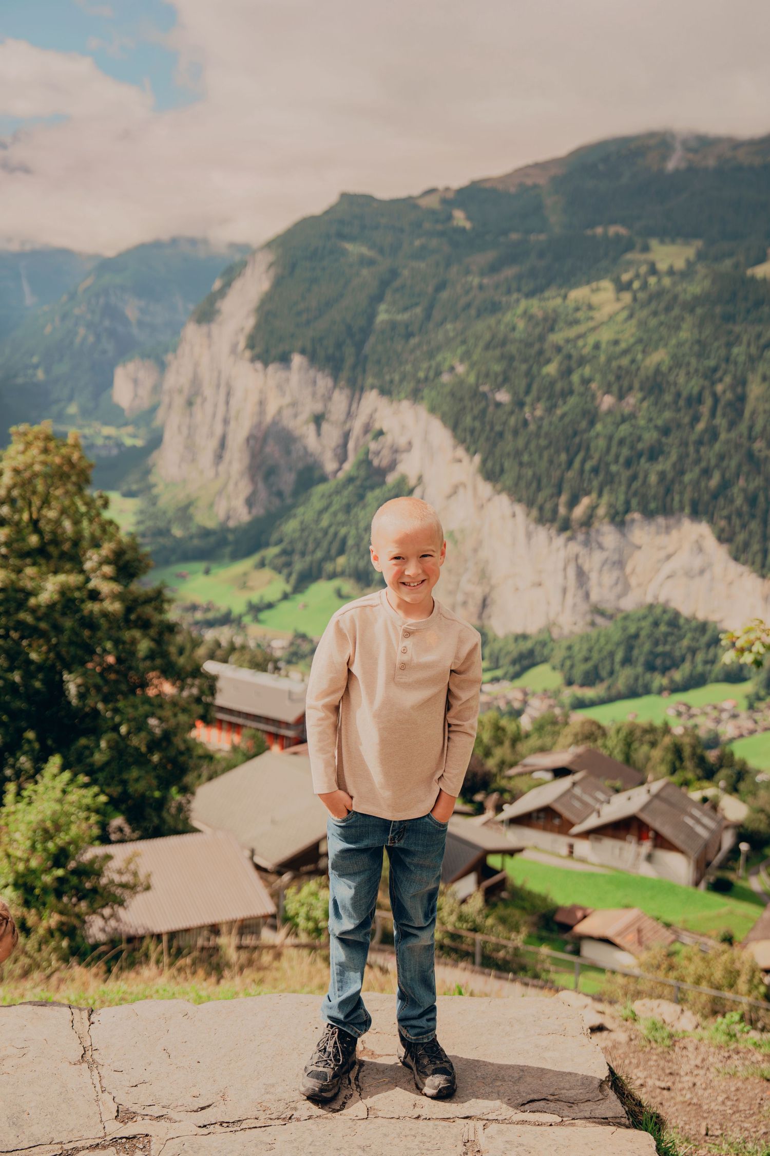 Happy young boy posing confidently with a breathtaking Swiss alpine village backdrop.