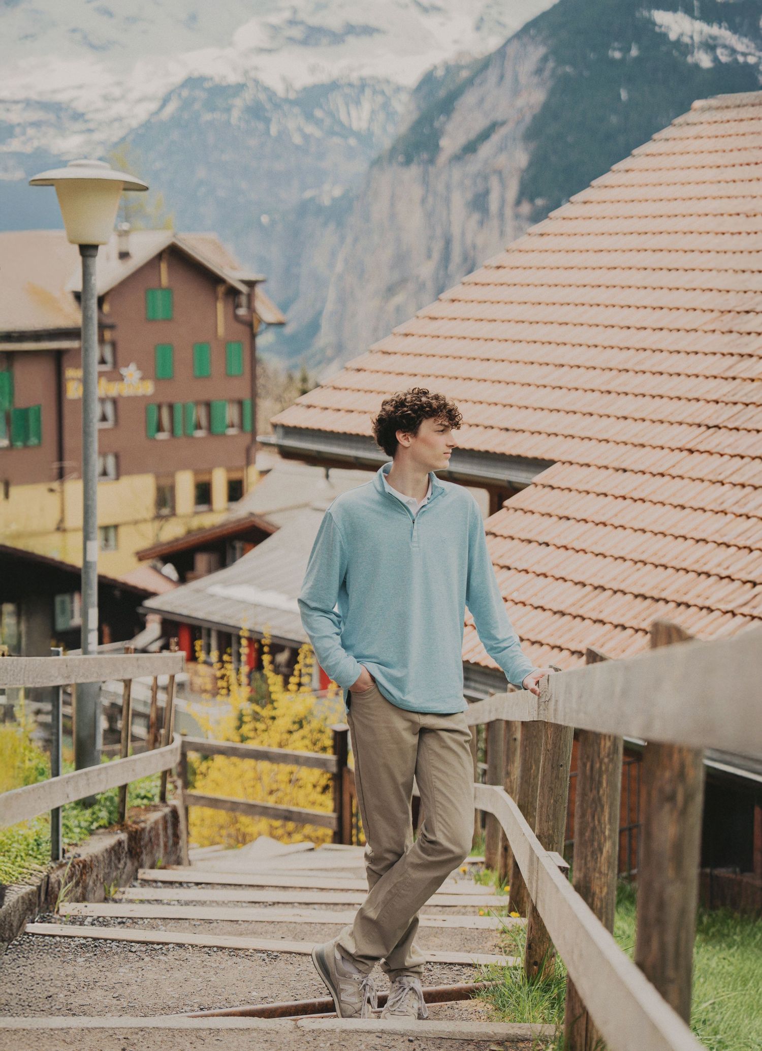 Teenage boy in light blue sweater standing on wooden steps in charming Swiss alpine village.