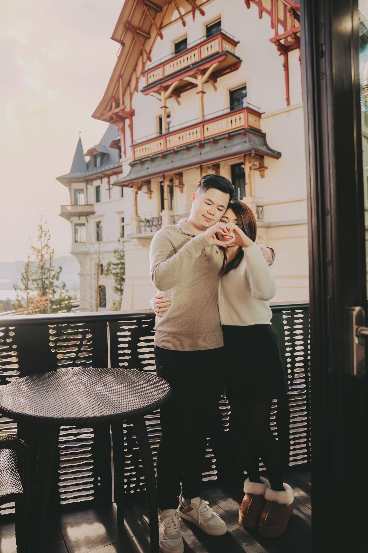 Couple making heart shape with hands on balcony of elegant European hotel.