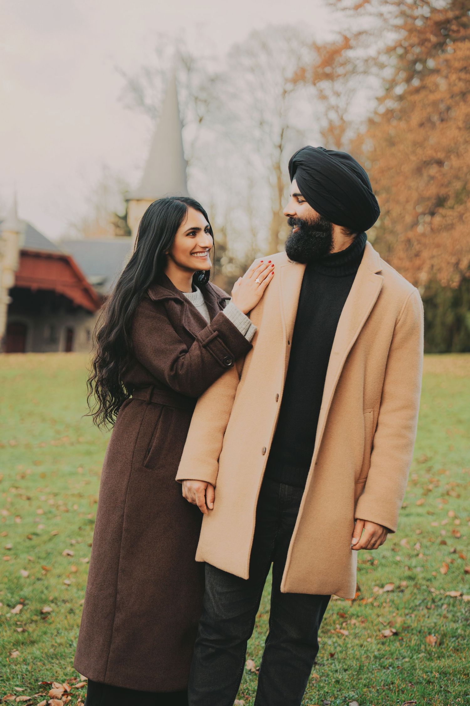 Couple smiling at each other in autumn park, woman touching mans coat.