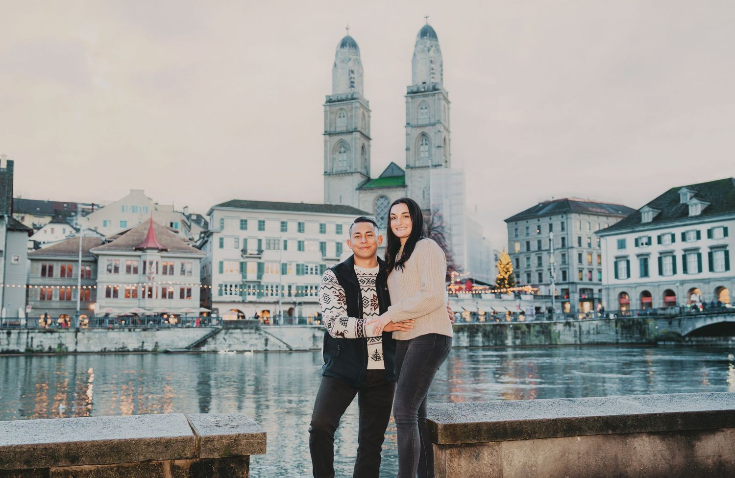 Couple embracing in front of Grossmünster church by the Limmat River in Zurich, Switzerland.