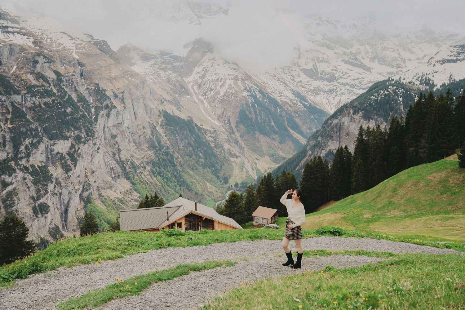 Person photographing dramatic snow-capped Swiss Alps landscape with alpine chalets and misty mountain peaks.