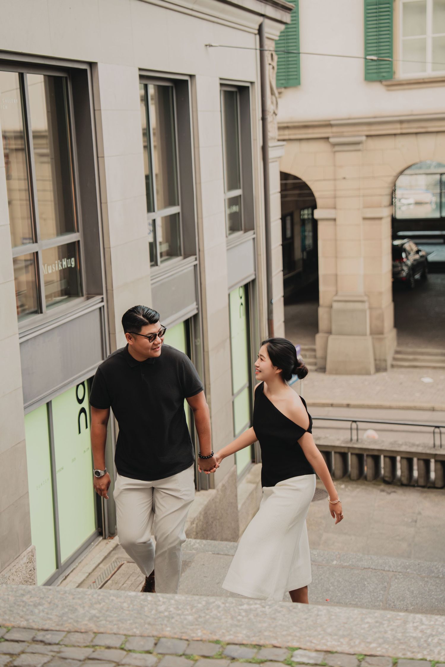 Smiling couple descending outdoor stairs hand in hand near a modern building in Zurich.