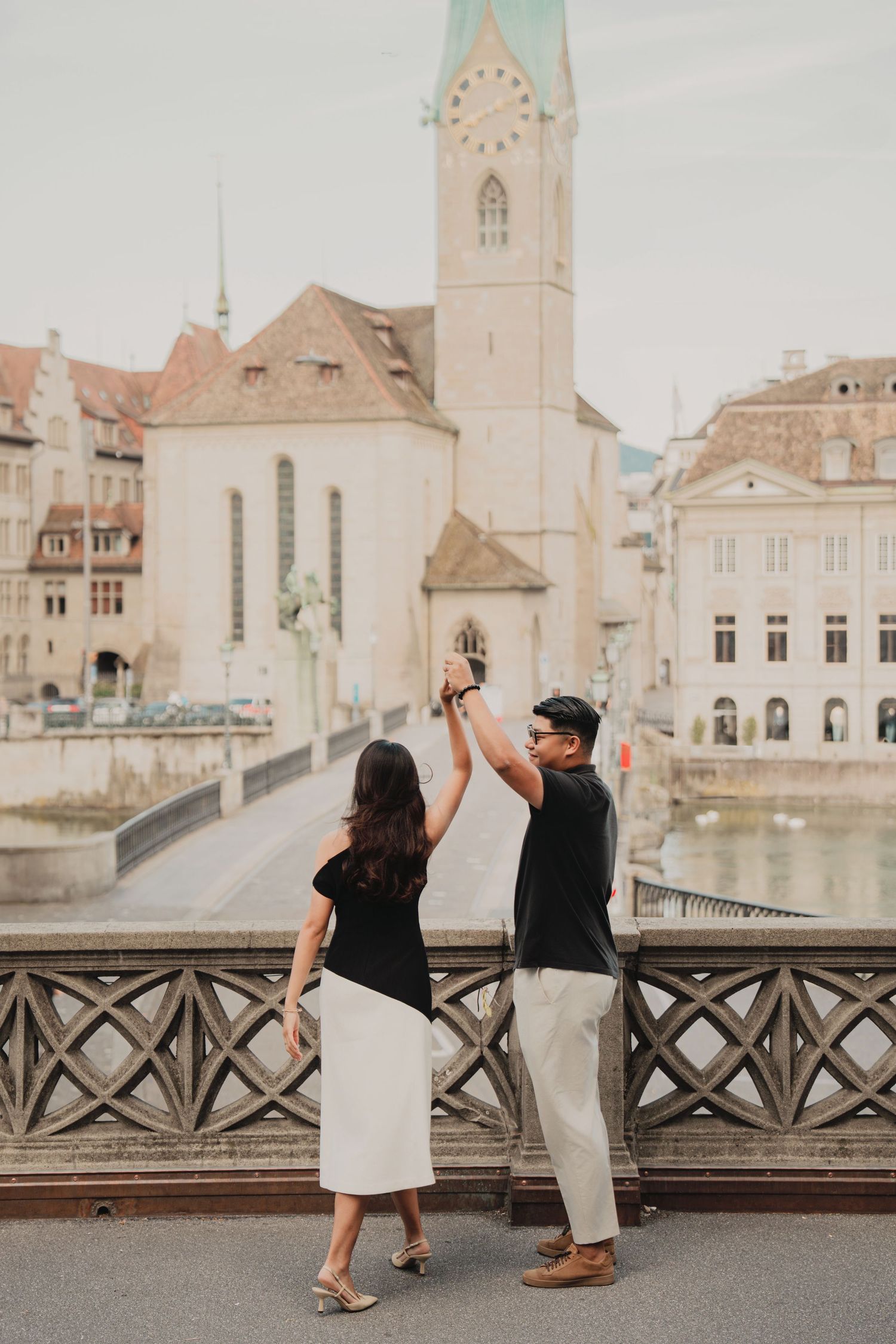Couple dancing on a bridge with Zurich old town and Fraumunster Church tower in the background.