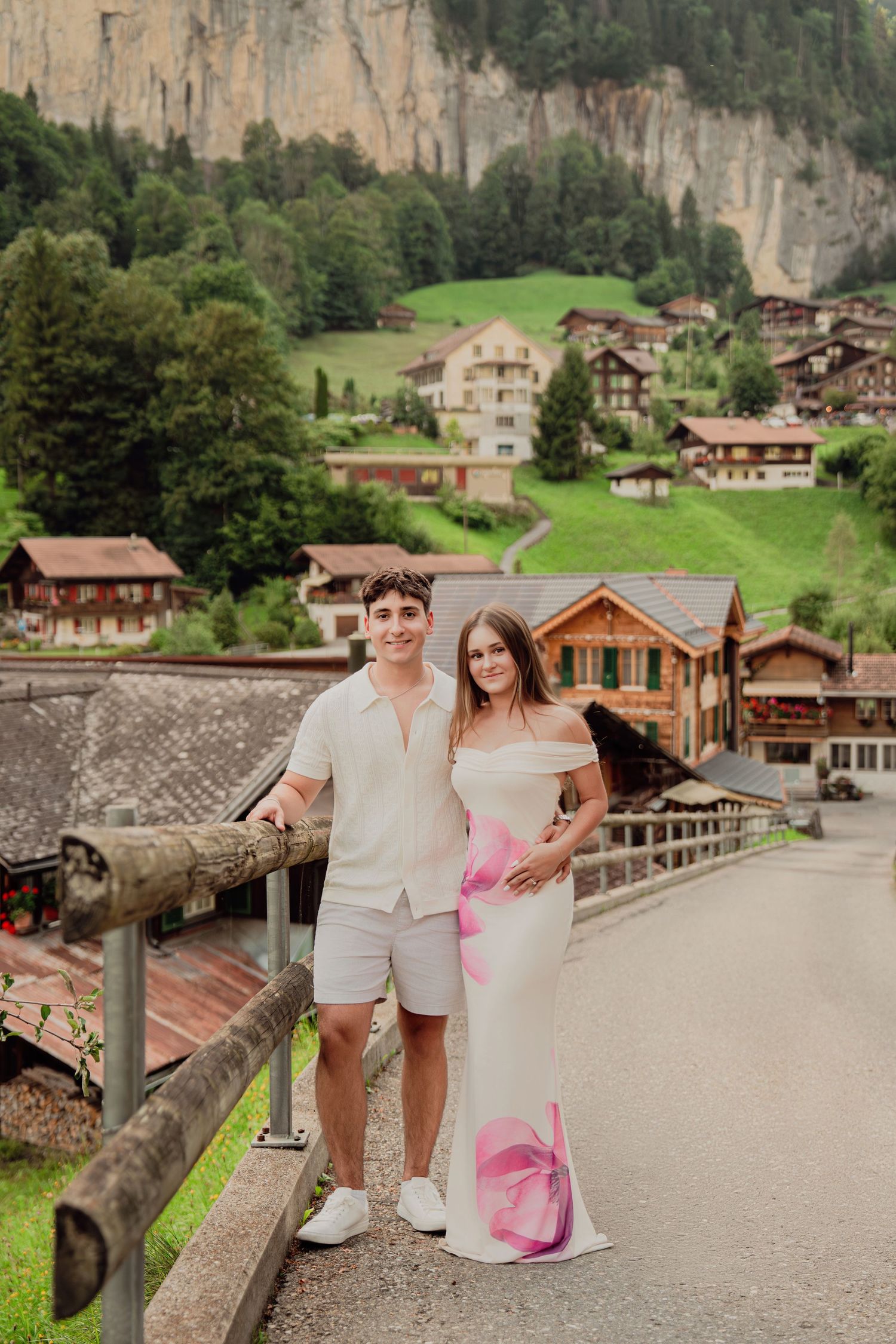 Stylish couple posing on bridge in Lauterbrunnen Switzerland with dramatic cliff and village view.