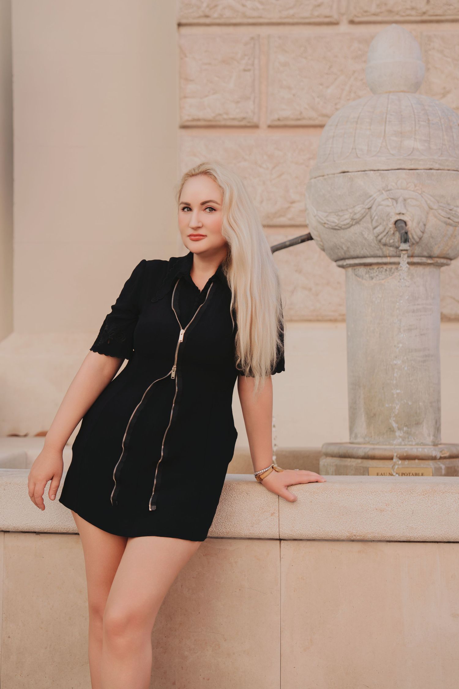 Blonde woman in black dress leaning against a decorative stone fountain in Monaco.