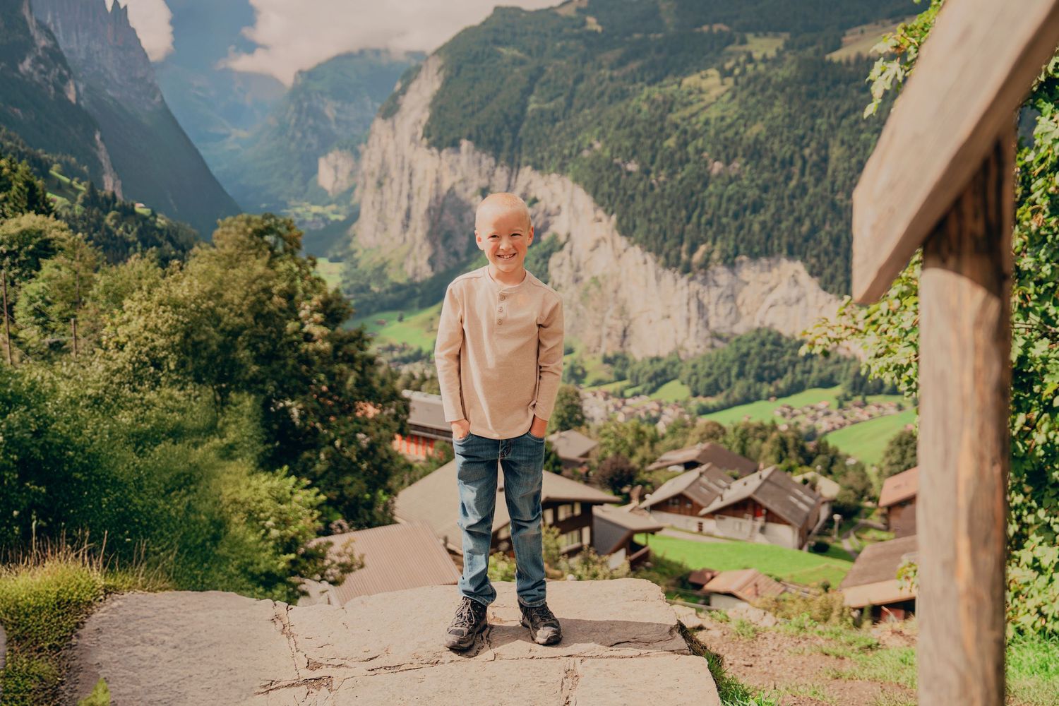 Smiling blonde boy standing on a stone path with Lauterbrunnen valley behind him.