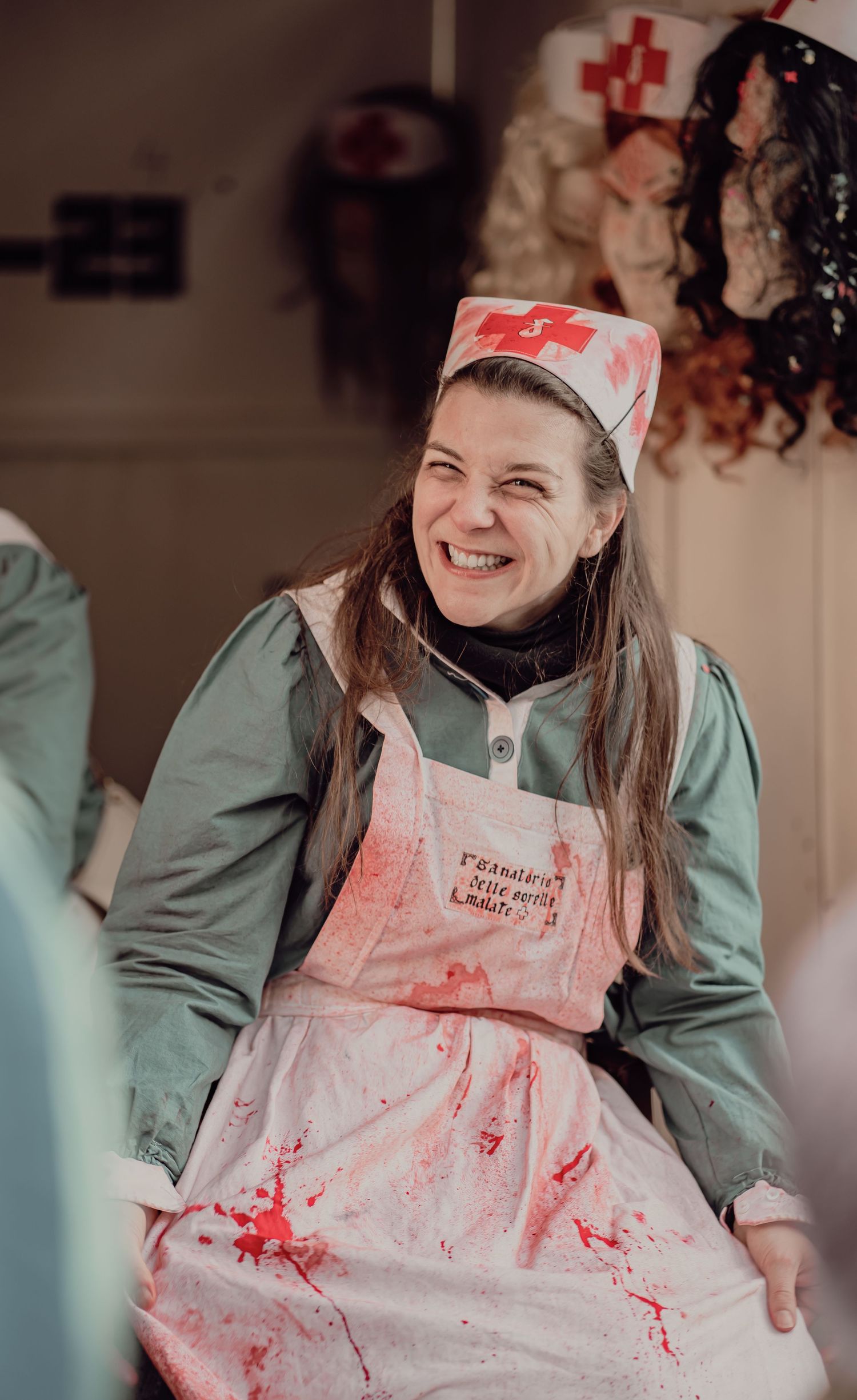 Smiling woman in bloody nurse Halloween costume with red cross hat at a festive event.
