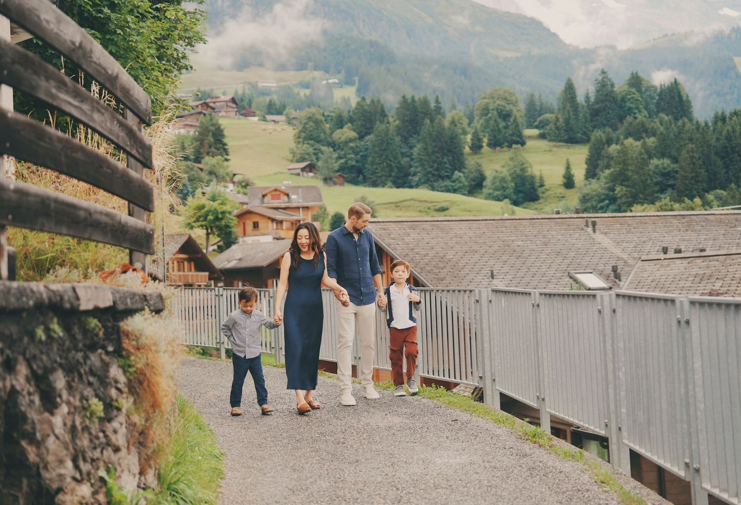 Young family of four walking hand in hand along a scenic path in a Swiss mountain village.