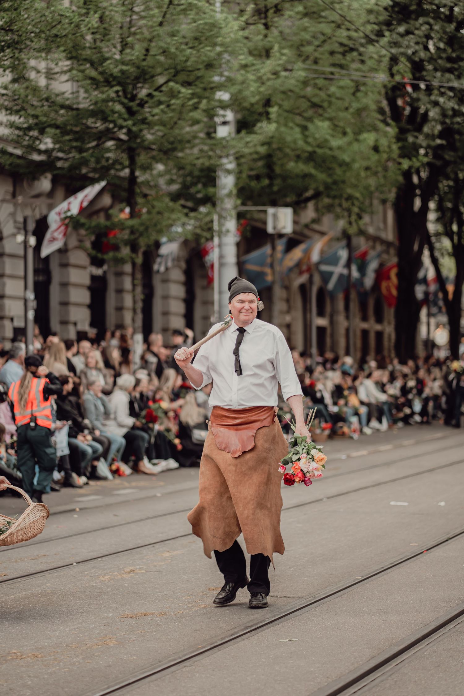 Man in traditional leather apron holding flowers and tool during street parade.