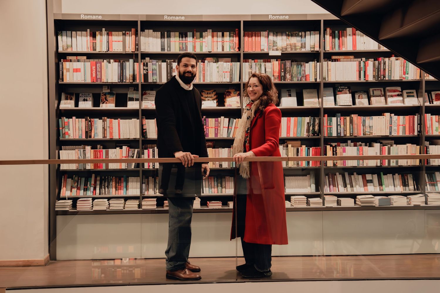 Man and woman standing together smiling in front of floor-to-ceiling bookshelves in a modern library.