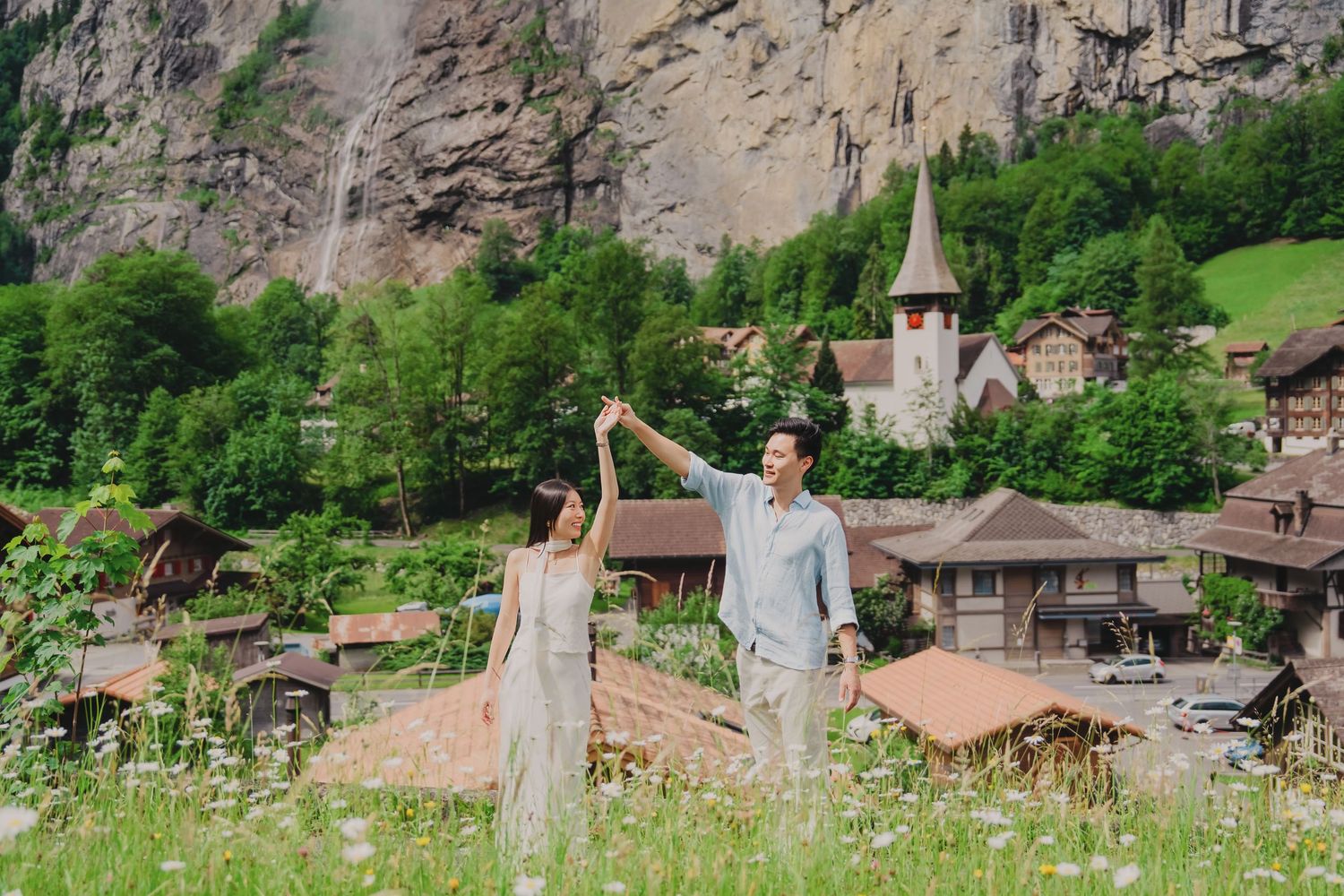 Couple dancing in a wildflower field with Lauterbrunnen waterfall and Swiss village in the background.