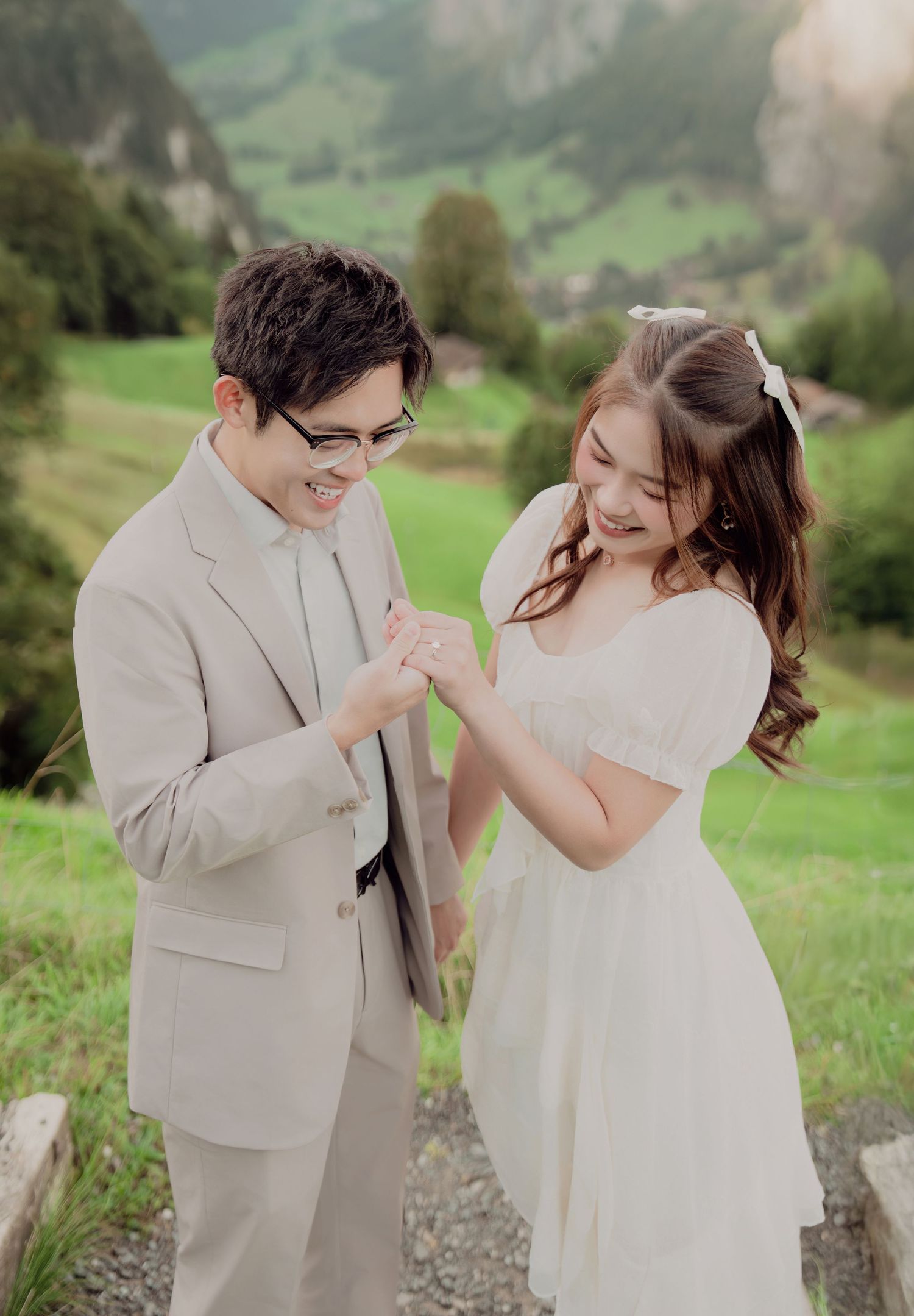 Happy couple laughing together in wedding attire on Swiss alpine meadow with green mountain backdrop.