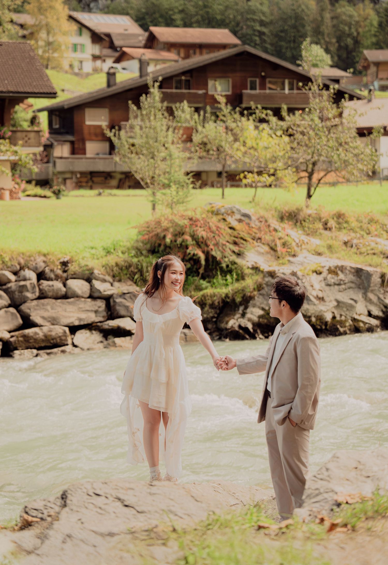 Couple holding hands on riverside rocks in a dreamy Swiss village setting in Lauterbrunnen, Switzerland.