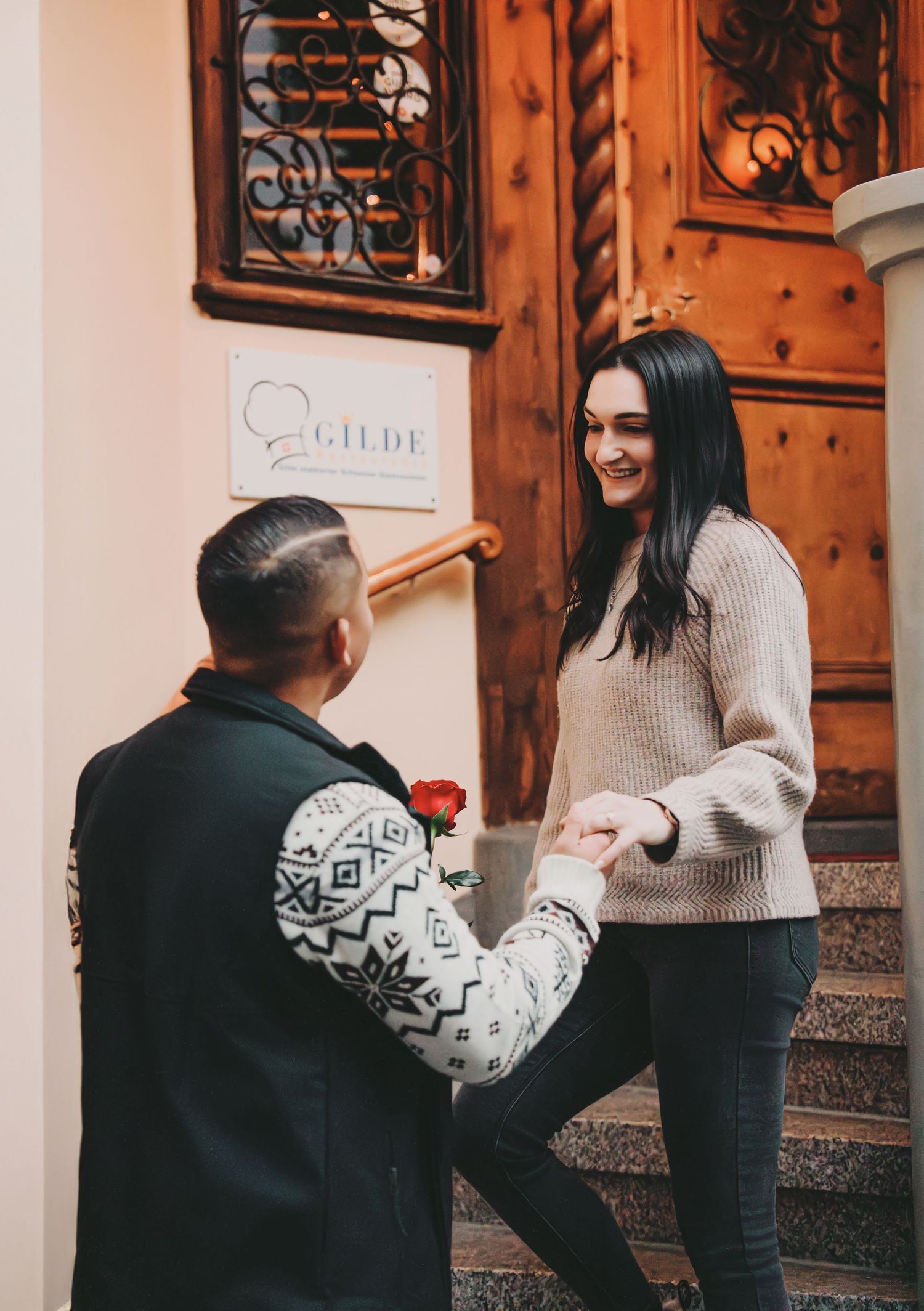 Man presenting a red rose to a smiling woman on steps outside a historic building in Zurich.
