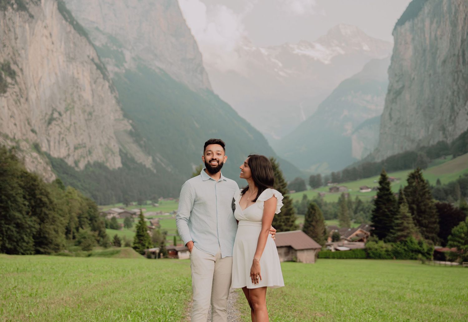 Happy couple standing together on a grassy field with a stunning Swiss mountain valley backdrop.