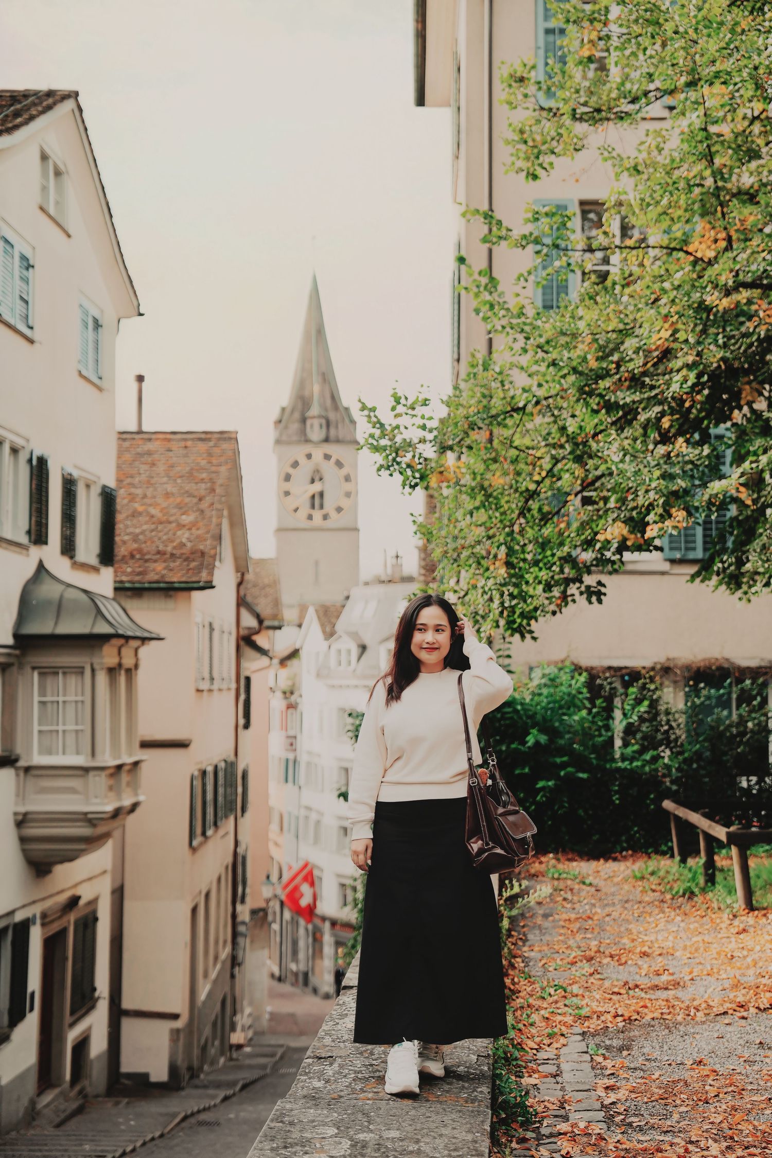 Young woman in white sweater and black skirt poses on cobblestone street in Zurich old town.