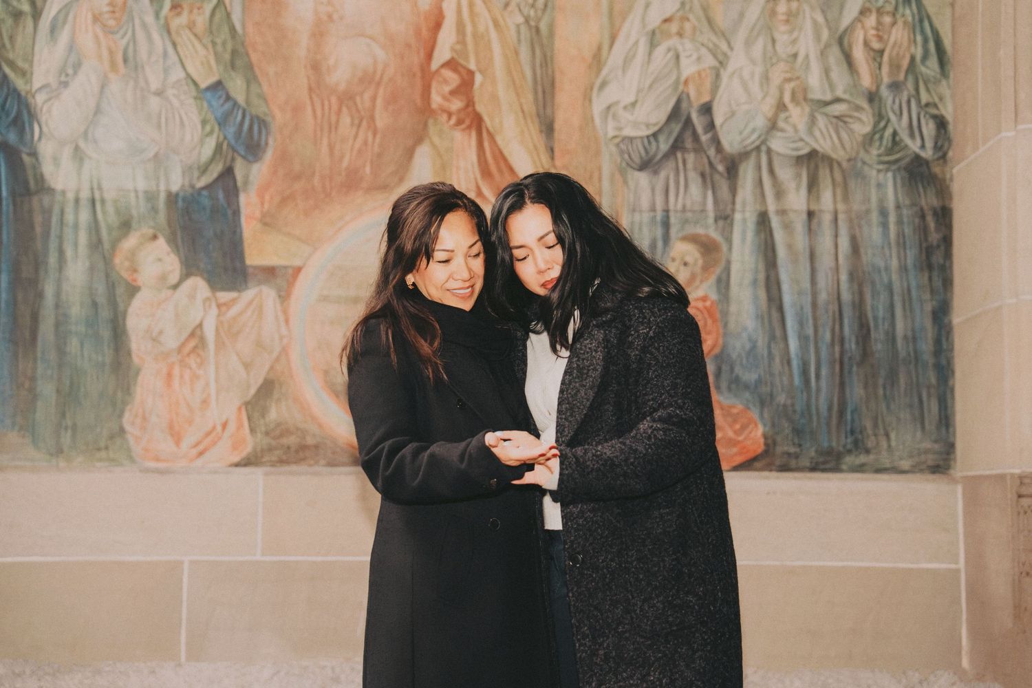 Two women looking at an engagement ring together in front of a decorative painted wall.