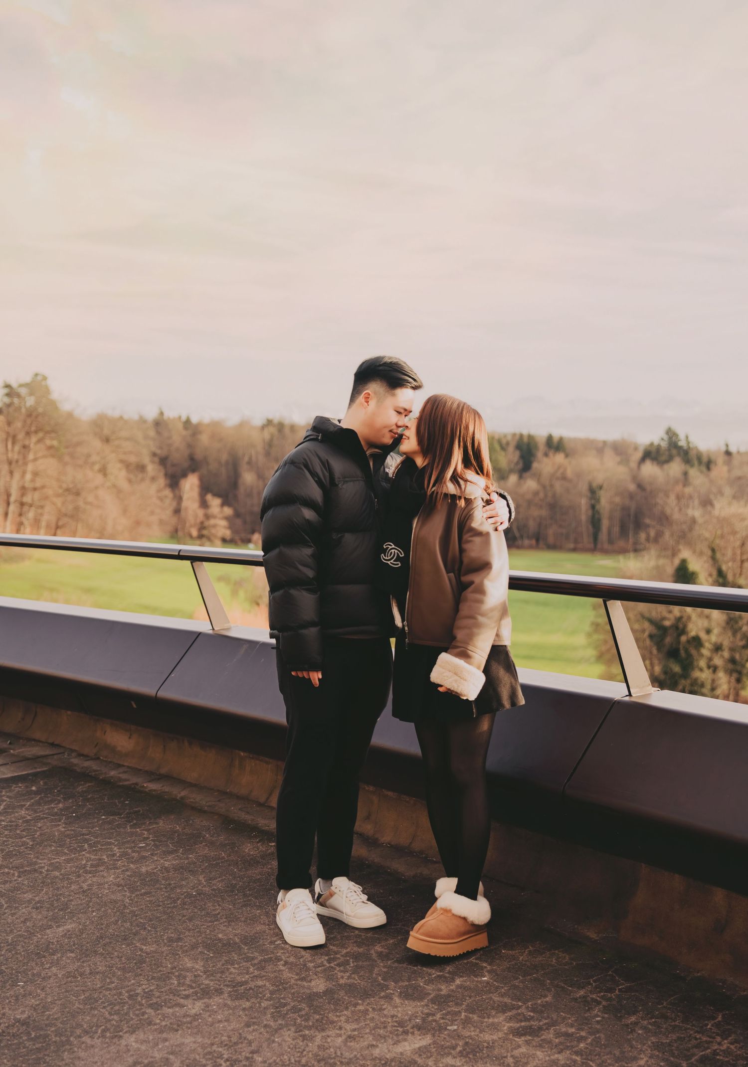 Asian couple sharing a kiss on a rooftop terrace with scenic green landscape behind them.