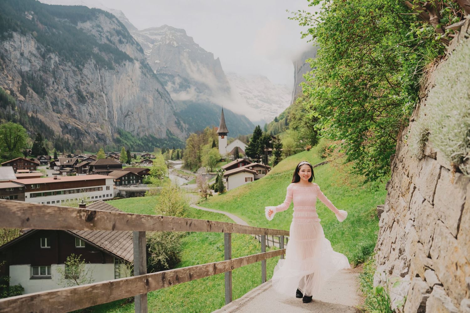 Woman in pink dress walking joyfully along path with stunning Swiss village of Lauterbrunnen in the background.