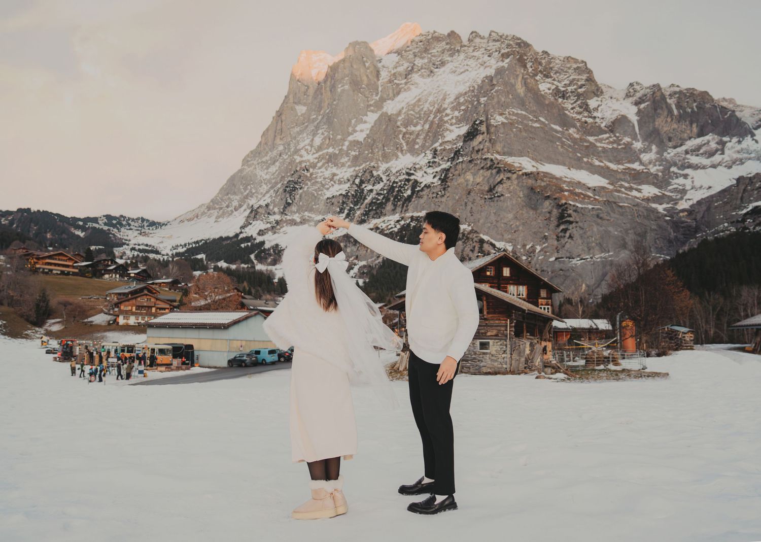 Couple dancing in snowy Dolomites village with dramatic mountain backdrop at sunset.