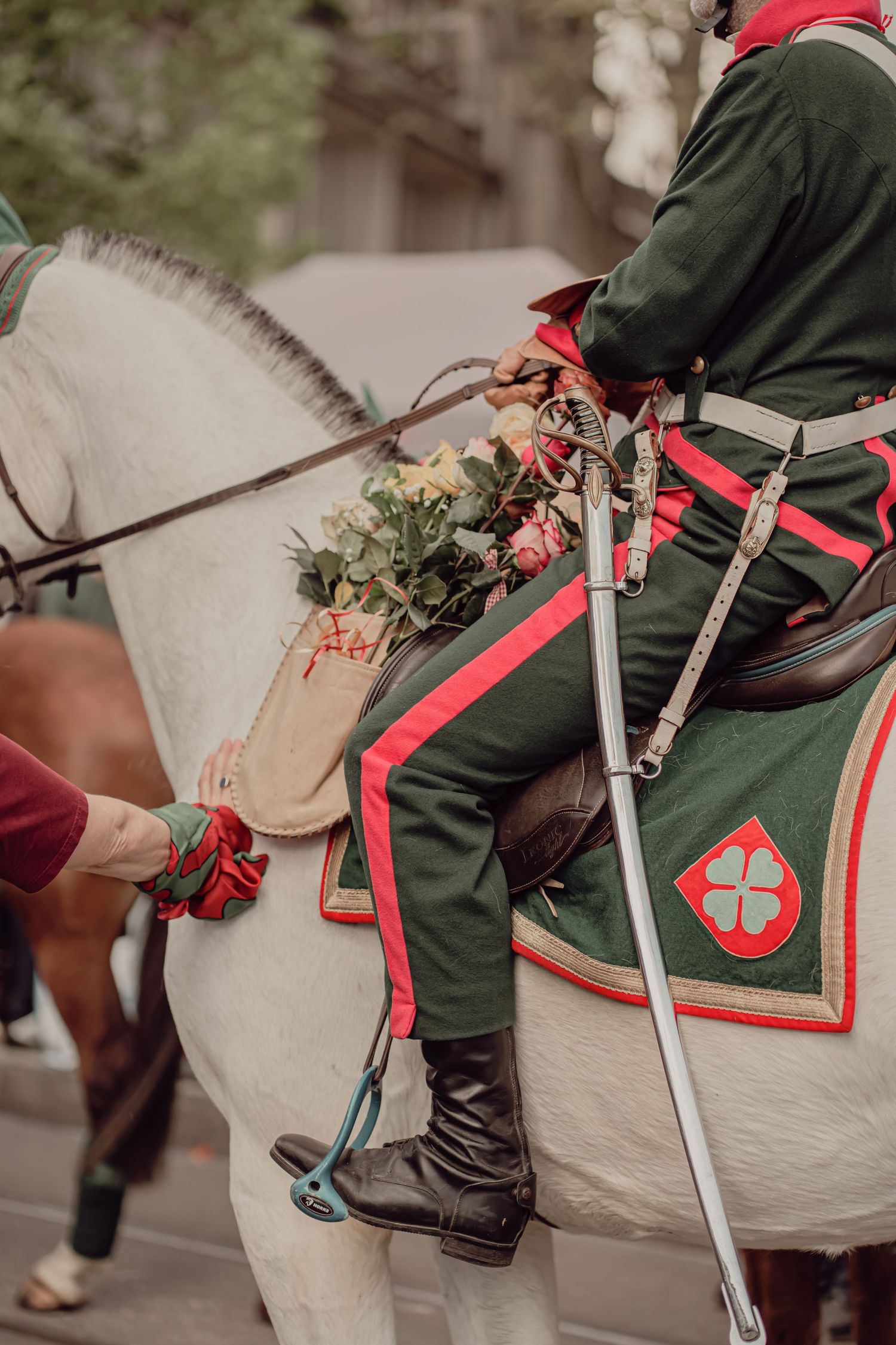 Rider in green military uniform on white horse carrying flowers in a parade.