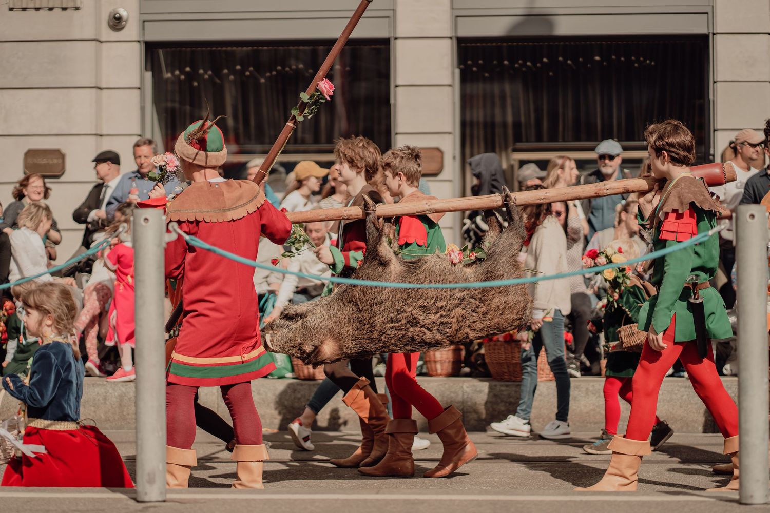 Performers in colorful medieval costumes carry a large log during a lively outdoor historical festival.
