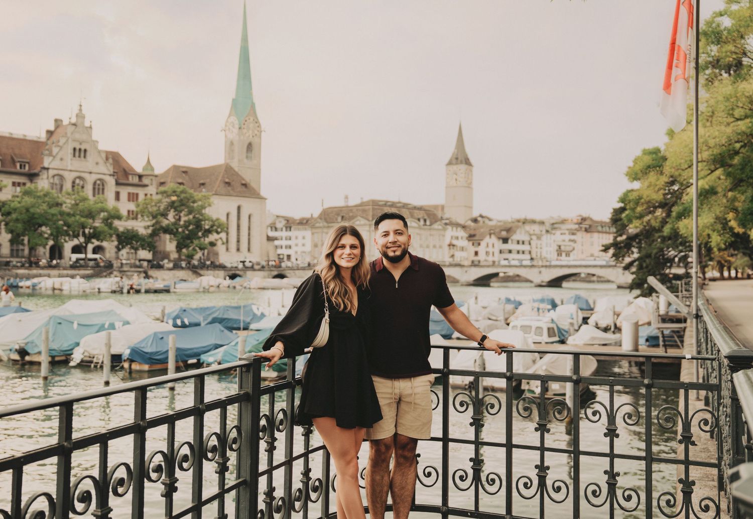 Couple posing together on a scenic Zurich waterfront balcony with church spires and river views.