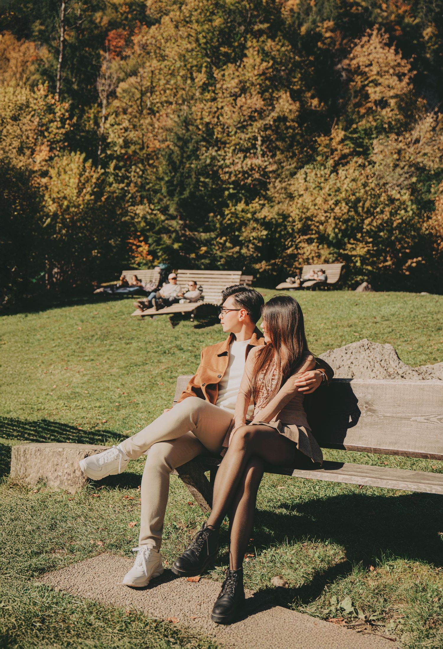 Couple sitting on a bench in a sunny autumn park surrounded by colorful fall foliage.