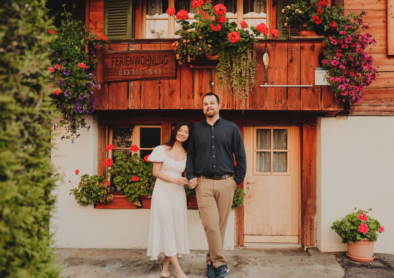 Smiling couple holding hands in front of a charming Swiss chalet with colorful flower boxes.