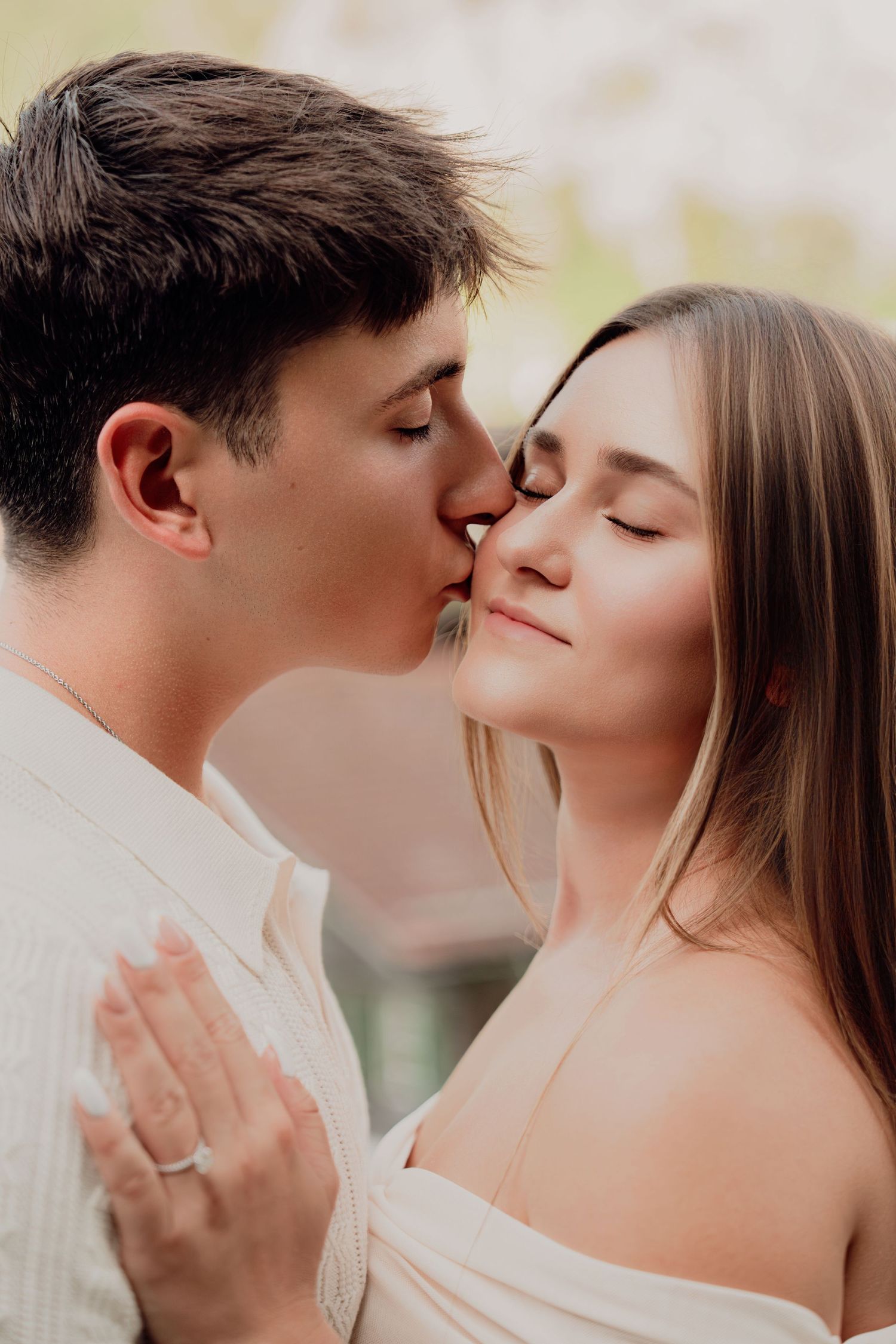 Close-up of a young couple sharing a tender kiss outdoors, woman wearing an engagement ring on her hand.