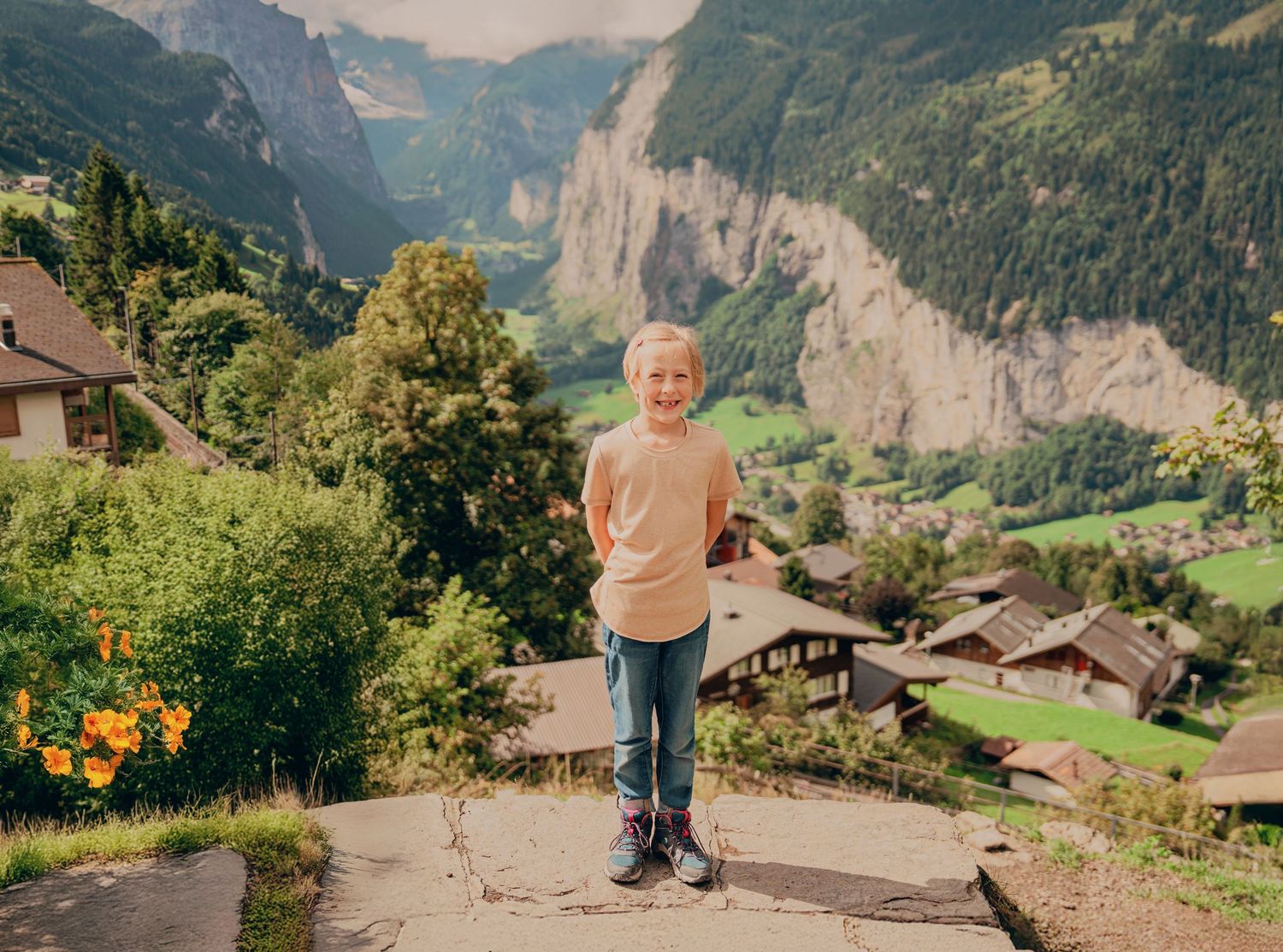 Smiling boy in yellow shirt and jeans standing on stone path with stunning Swiss Alpine valley view.
