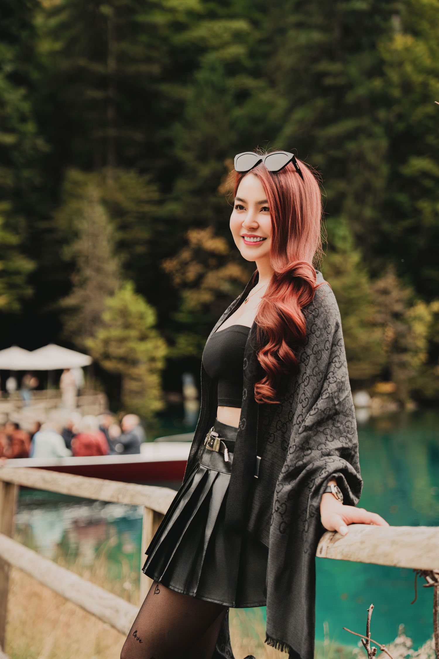 Smiling red-haired woman in black outfit with gray shawl posing by turquoise alpine lake.