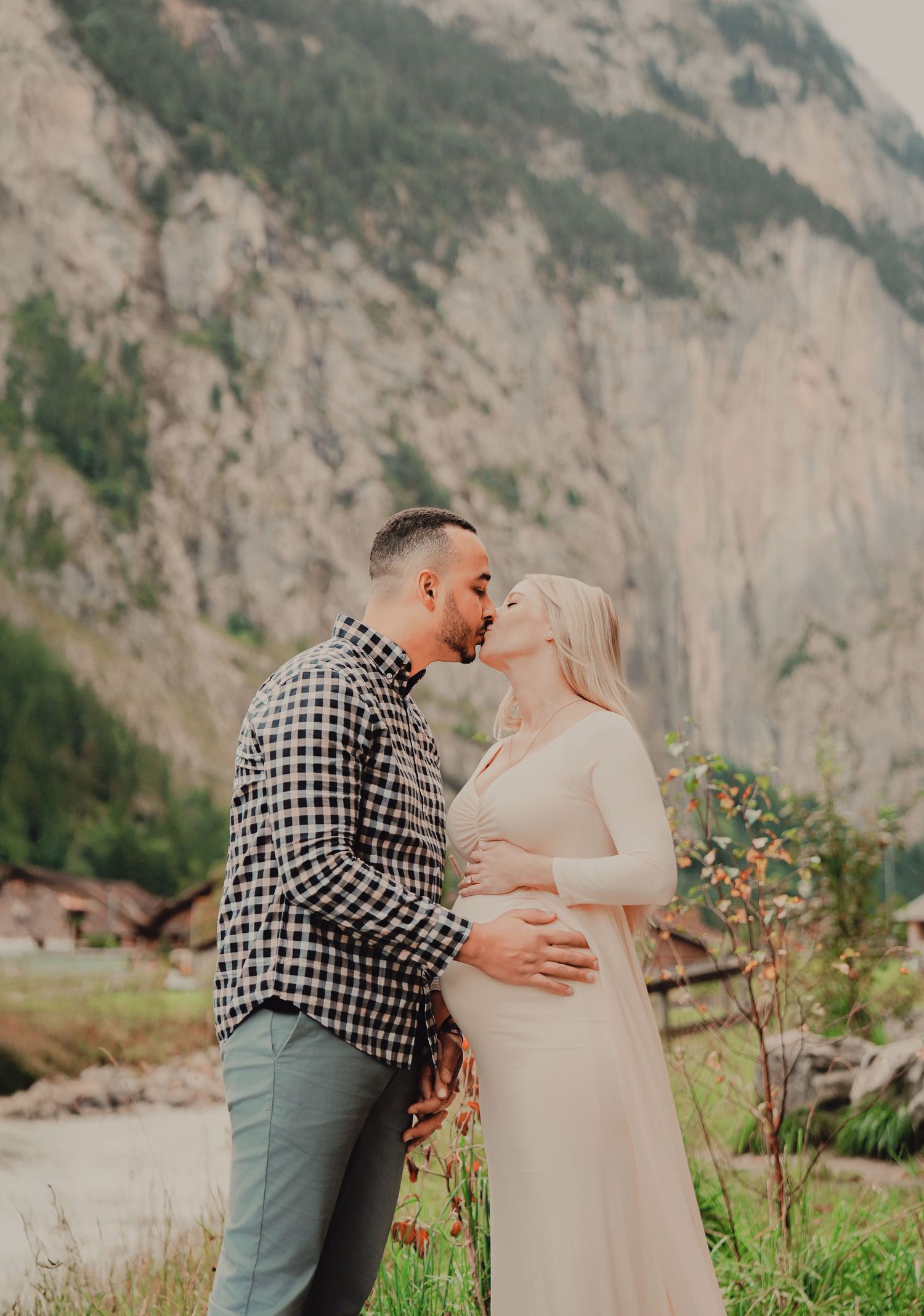 Couple sharing a kiss outdoors with towering Swiss mountain cliffs and waterfall in background.