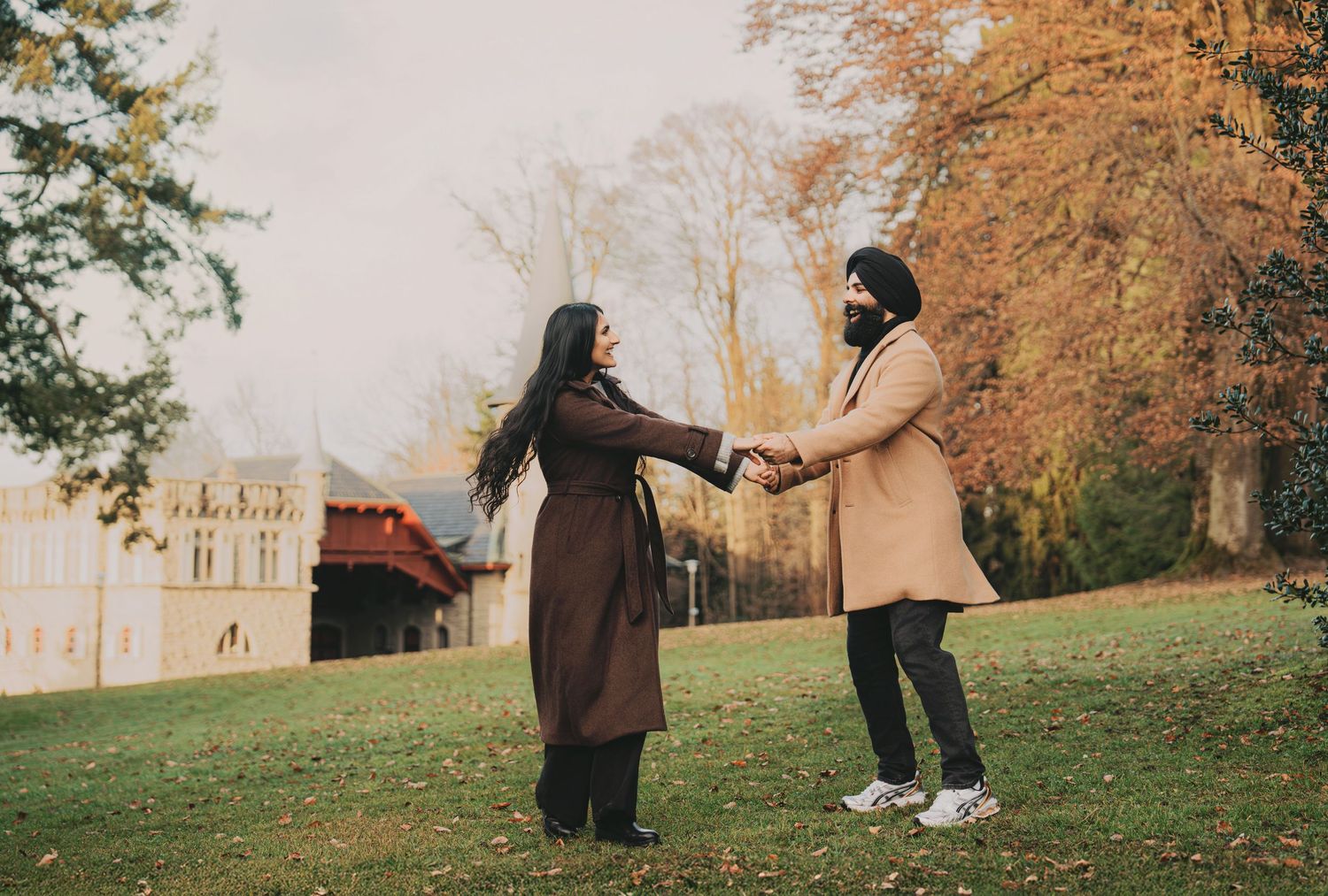 Couple holding hands facing each other on green lawn with fall foliage.