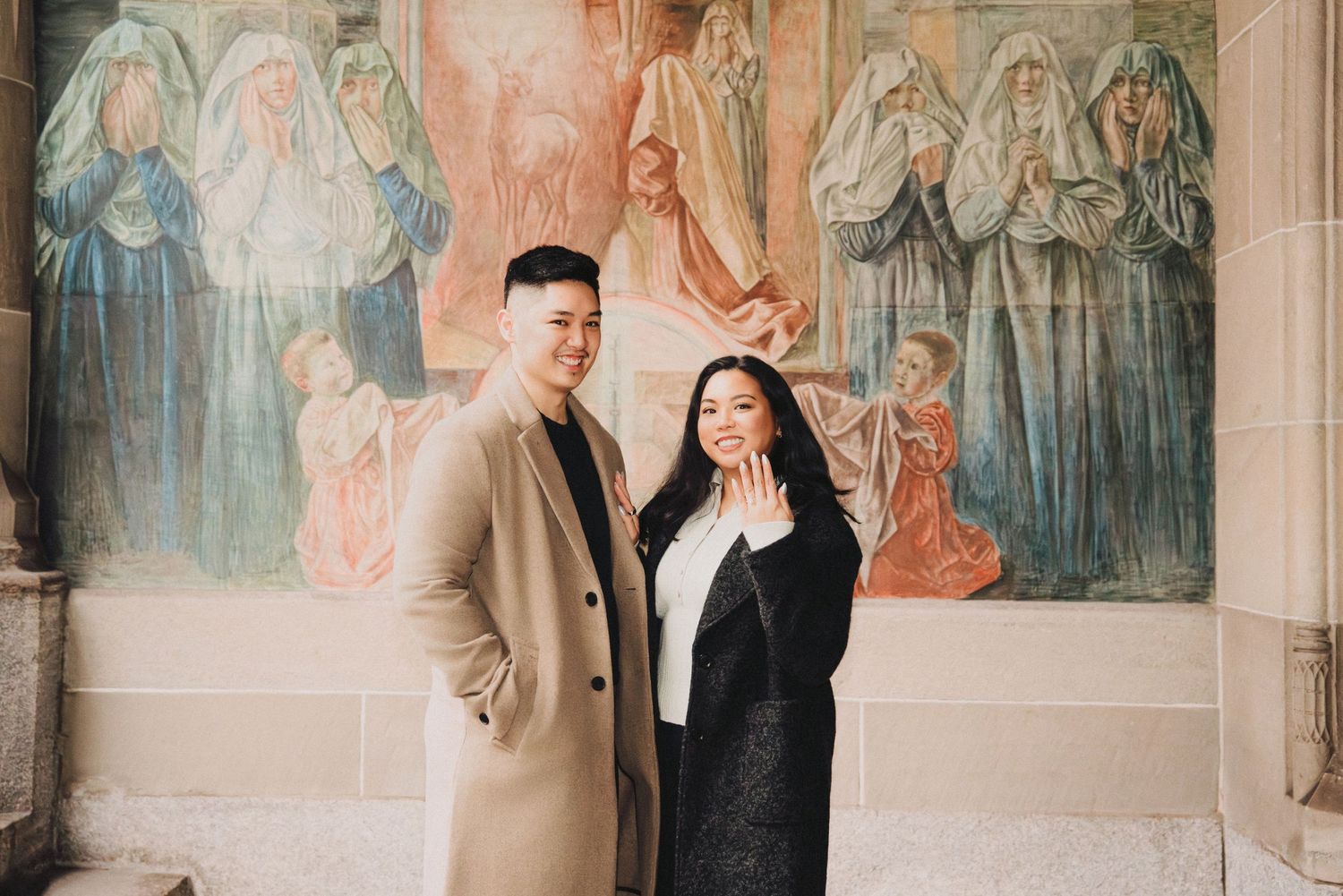 Engaged couple smiling together in front of a vibrant religious mural inside a cathedral.