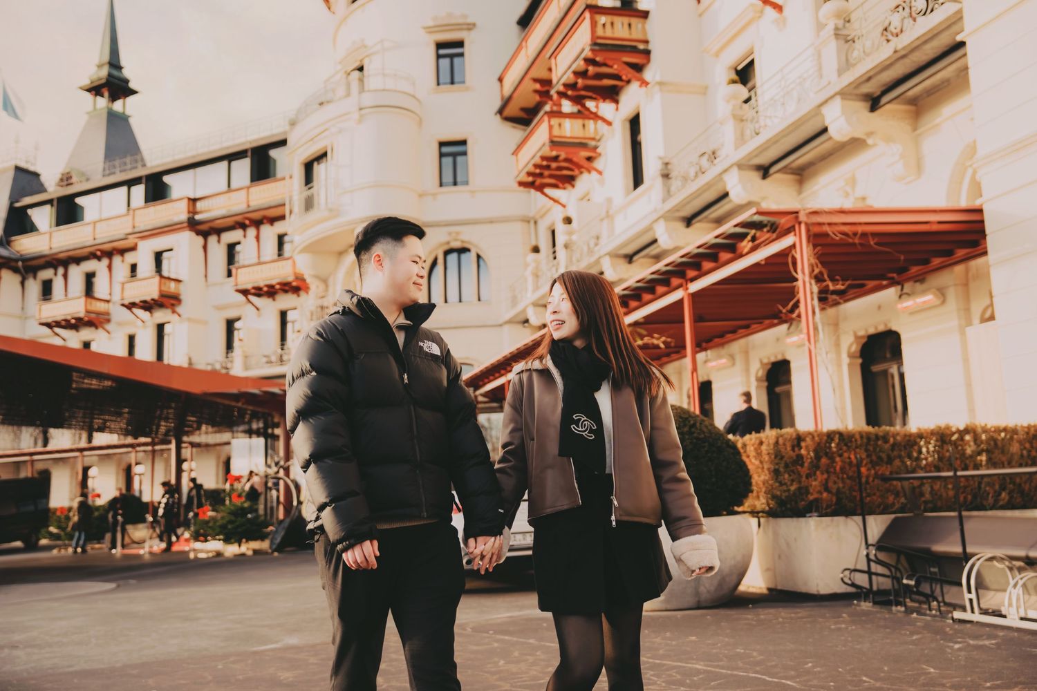 Asian couple holding hands and walking outside ornate European hotel building.